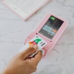 Hand using a contactless card on a pink POS terminal for a wireless transaction.