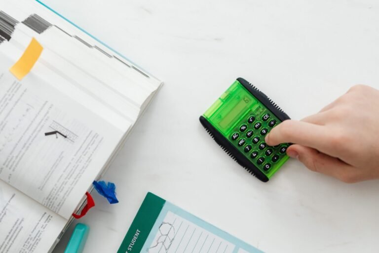 A student uses a green calculator to solve math equations from a textbook on a desk.
